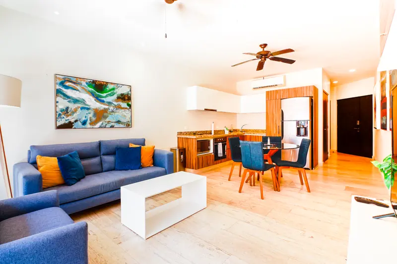Sala con sofá azul, comedor redondo y cocina integrada de la unidad 405